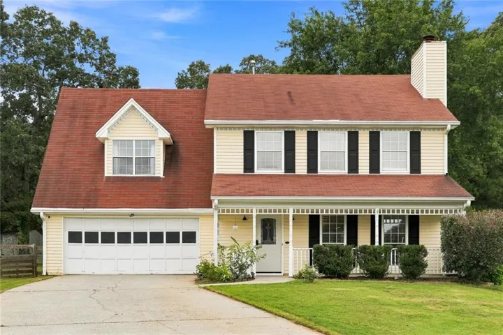 Two-story residence featuring light yellow siding, a prominent red roof, and a covered front porch