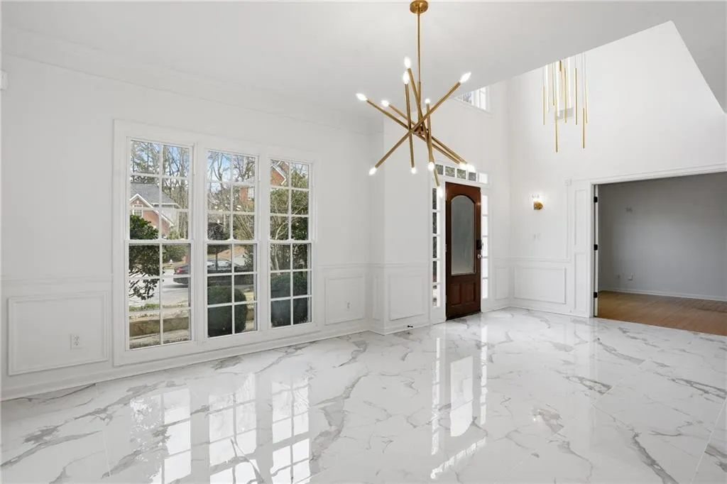 Unfurnished dining area featuring plenty of natural light, suspended lighting, a high ceiling, wainscoting, and light marble finish flooring