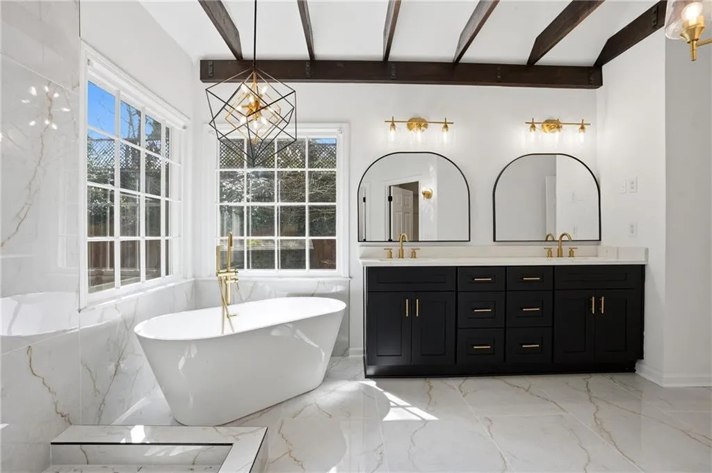 Bathroom with double vanity, a freestanding tub, light marble finish flooring, and beam ceiling