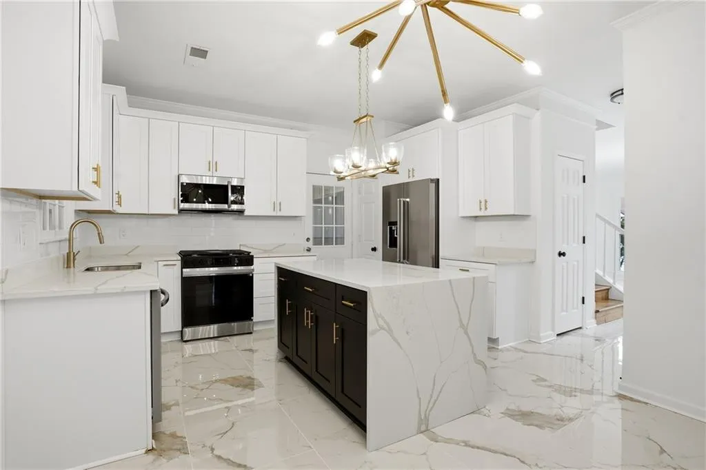 Kitchen featuring light stone countertops, stainless steel appliances, crown molding, two tone cabinets, and light marble finish flooring