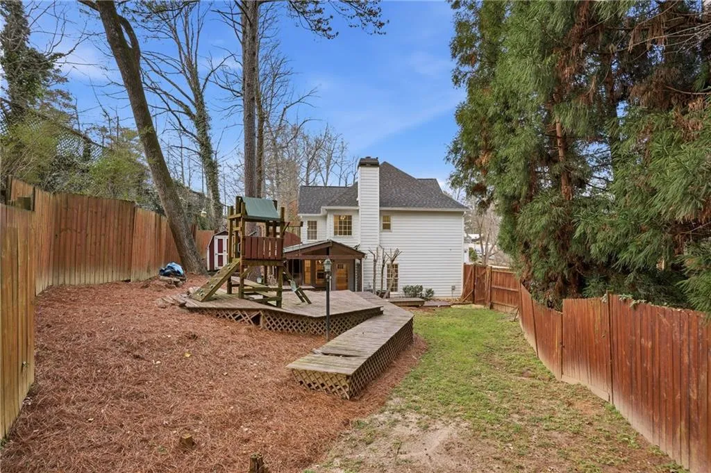 Rear view of house with a fenced backyard, a chimney, a deck, a shingled roof, and a playground