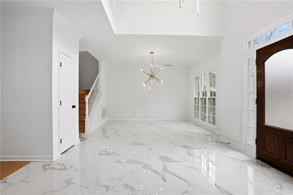 Entrance foyer with a decorative wall, suspended lighting, crown molding, and a wainscoted wall