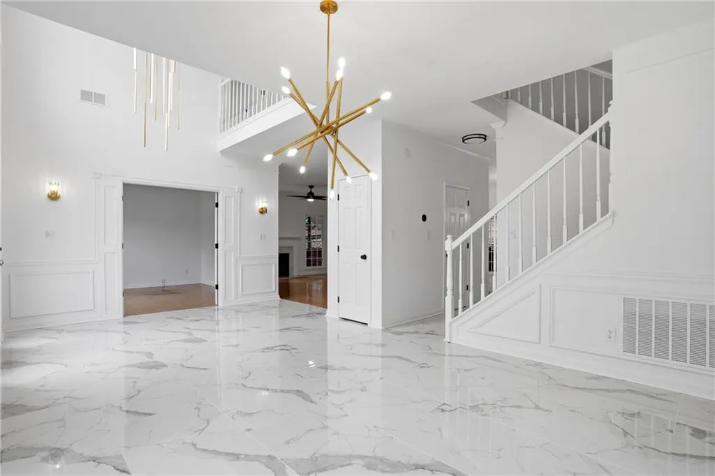 Unfurnished living room with a decorative wall, suspended lighting, a wainscoted wall, a high ceiling, and a fireplace