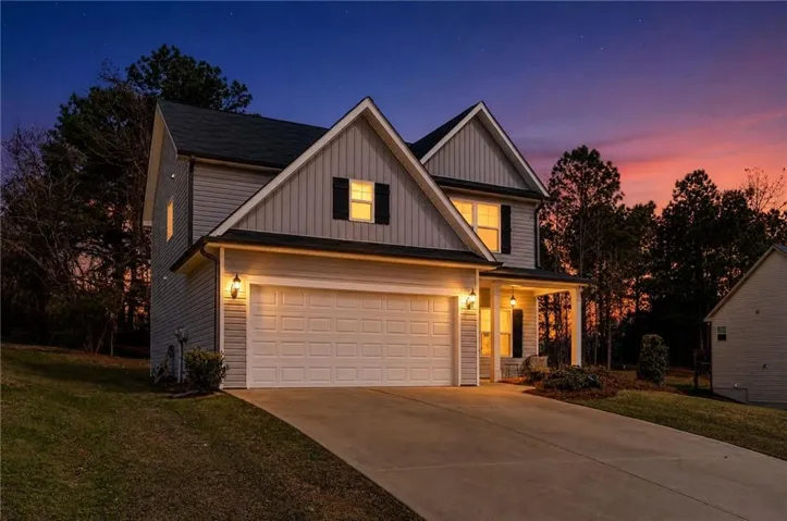 Modern two-story colonial featuring a two-car garage with illuminated exterior lighting, metal roof accents, and board-and-batten siding