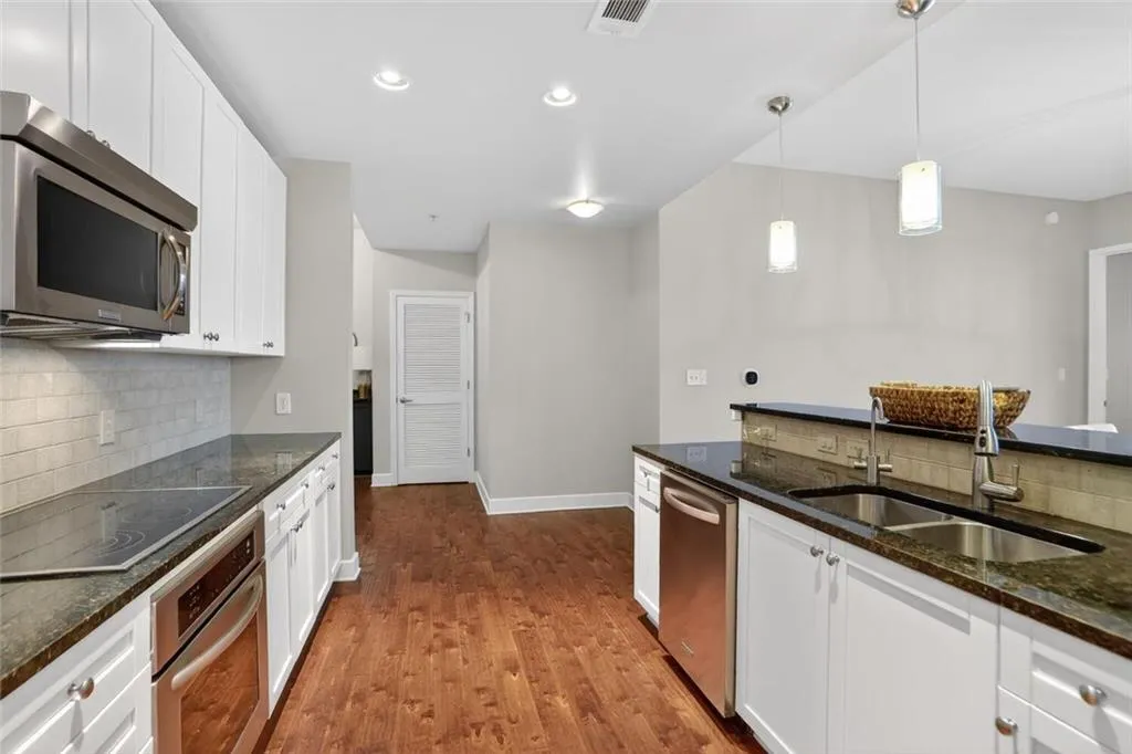 Kitchen featuring stainless steel appliances, dark stone countertops, pendant lighting, decorative backsplash, and white cabinets