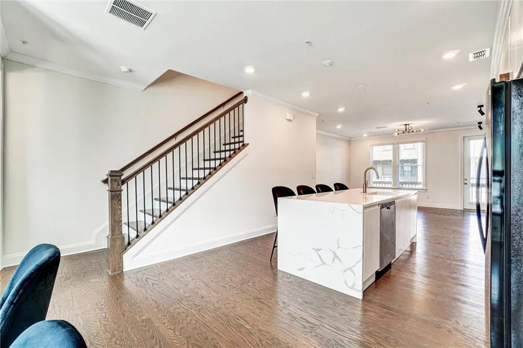 Kitchen featuring light stone countertops, ornamental molding, dark wood-type flooring, freestanding refrigerator, and a center island with sink