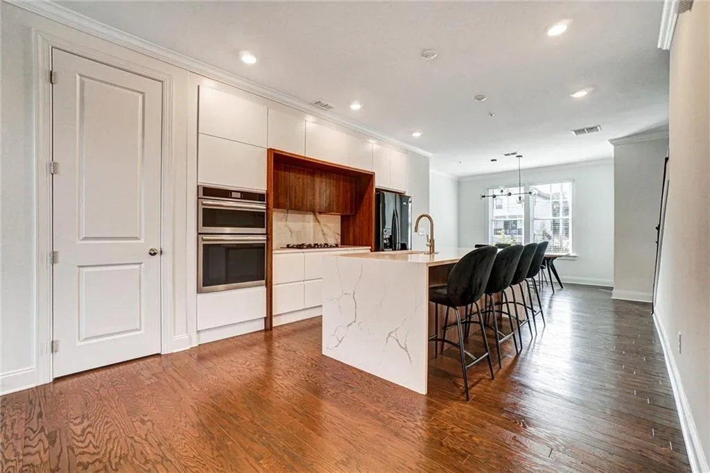 Kitchen with ornamental molding, modern cabinets, a breakfast bar area, a center island with sink, and light stone counters