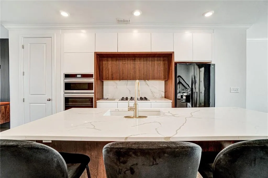 Kitchen with a kitchen breakfast bar, light stone countertops, black refrigerator with ice dispenser, double oven, and crown molding