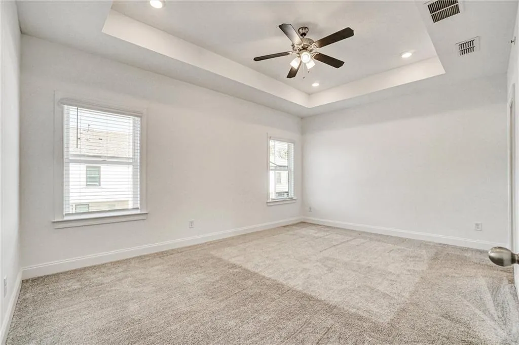 Empty room featuring a raised ceiling, light colored carpet, recessed lighting, and ceiling fan