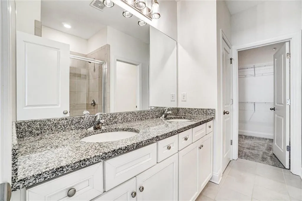 Full bathroom with double vanity, light tile patterned floors, a shower stall, and a spacious closet