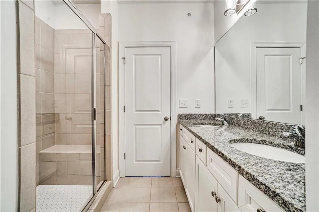 Full bathroom with double vanity, light tile patterned floors, and a shower stall