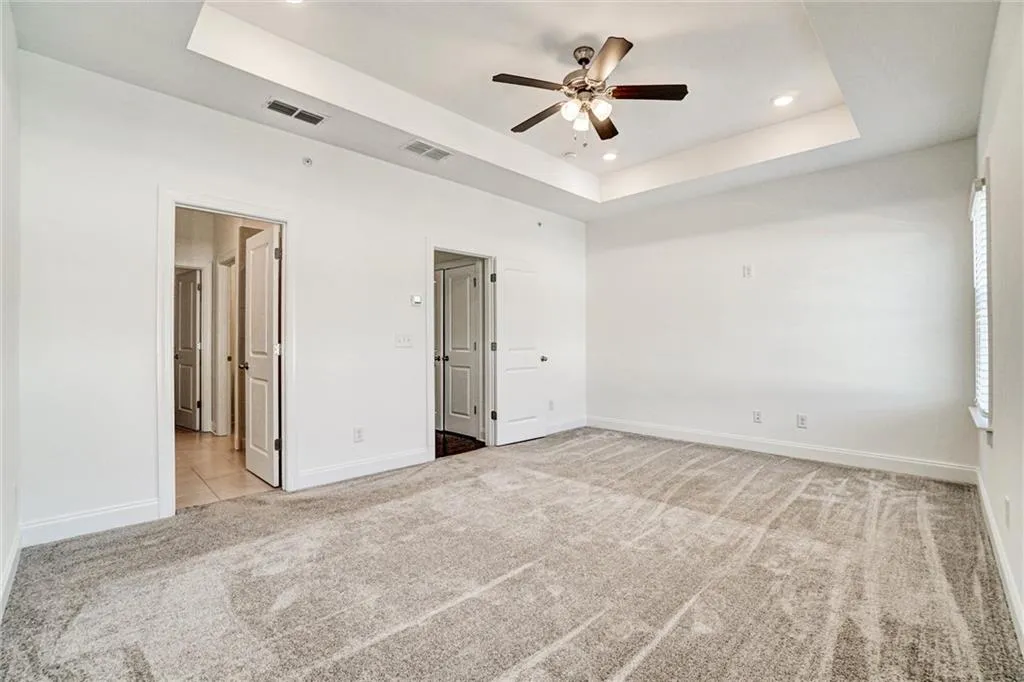 Unfurnished bedroom with a tray ceiling, light carpet, ceiling fan, and recessed lighting