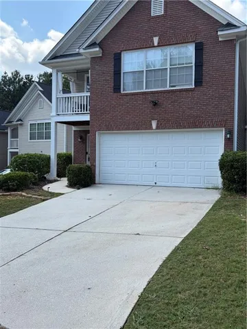 Brick exterior with white trim, two-car garage, upper-level balcony, and a concrete driveway