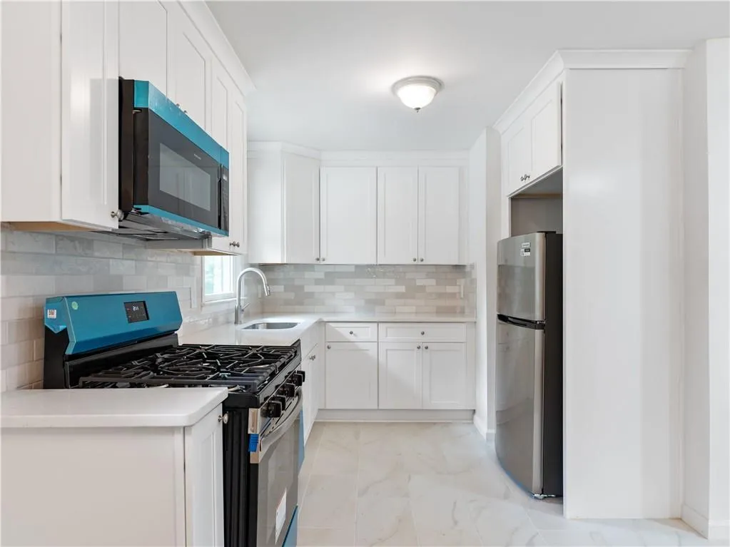 Kitchen featuring gas stove, freestanding refrigerator, white cabinetry, light stone counters, and decorative backsplash