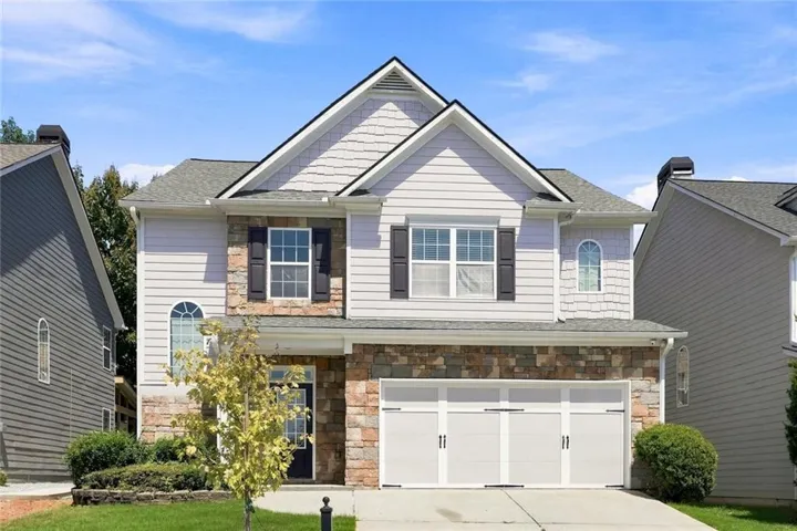 Two-story residence featuring a stone and siding facade, a two-car garage, and an arched window detail