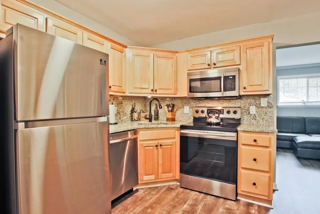 Kitchen featuring appliances with stainless steel finishes, light brown cabinetry, light wood-style floors, decorative backsplash, and light stone counters
