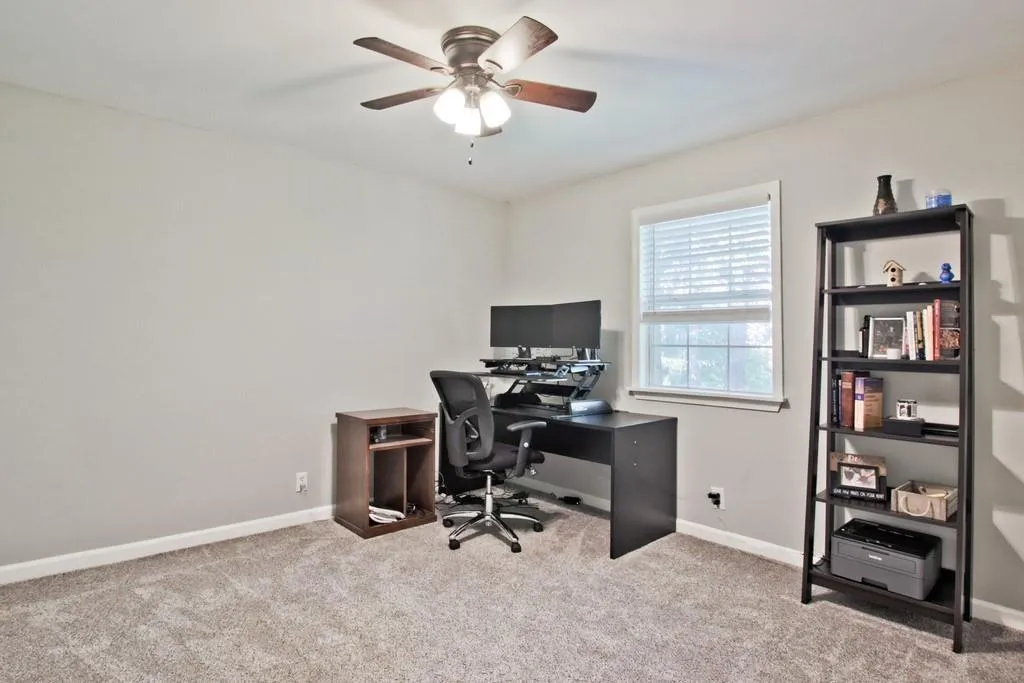Carpeted office with a ceiling fan and baseboards