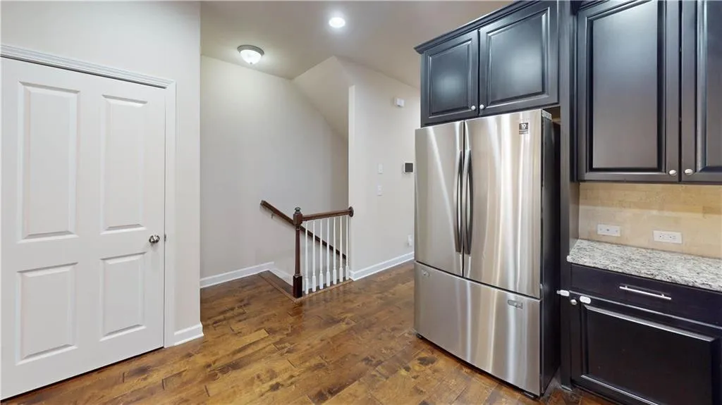 Kitchen featuring decorative backsplash, stainless steel fridge, light stone countertops, and dark hardwood / wood-style flooring