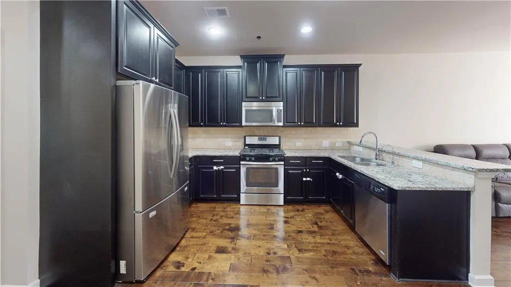 Kitchen featuring kitchen peninsula, appliances with stainless steel finishes, light stone countertops, dark hardwood / wood-style floors, and sink