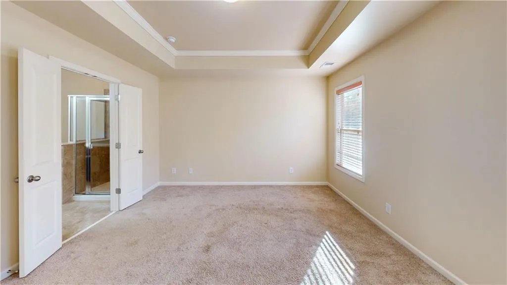 Master bedroom with crown molding, a tray ceiling, and light colored carpet