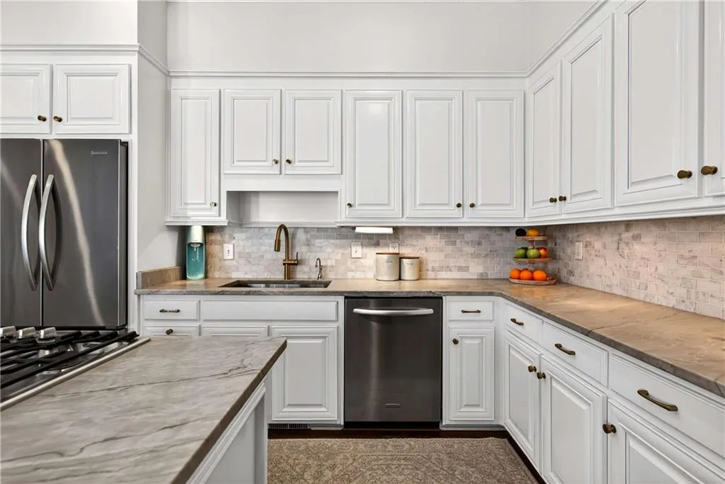 The kitchen is both stylish and welcoming, featuring stone countertops and a coordinating stone backsplash that add texture and timeless appeal.