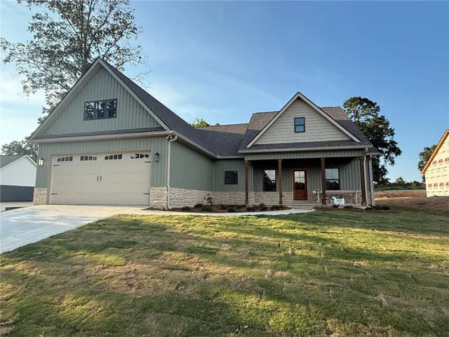 Modern farmhouse residence showcasing a spacious two-car garage with paneled overhead doors, freshly poured concrete driveway, and gable-roof architecture with board-and-batten exterior siding