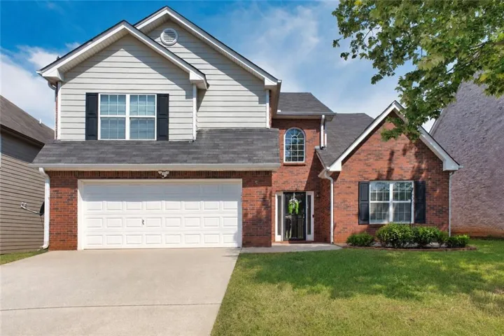Brick and siding exterior with a two-car garage, arched window, manicured shrubs, and a concrete driveway