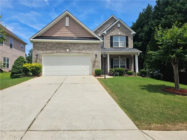 Traditional two-story home featuring a brick facade with shuttered windows, a covered front porch, and an attached two-car garage