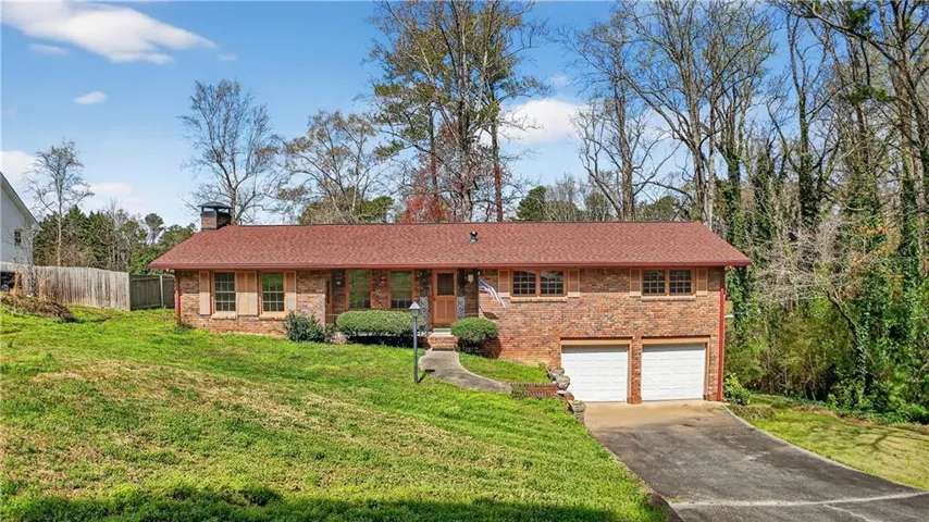 Brick exterior with a red shingle roof, attached two-car garage, and established front landscaping
