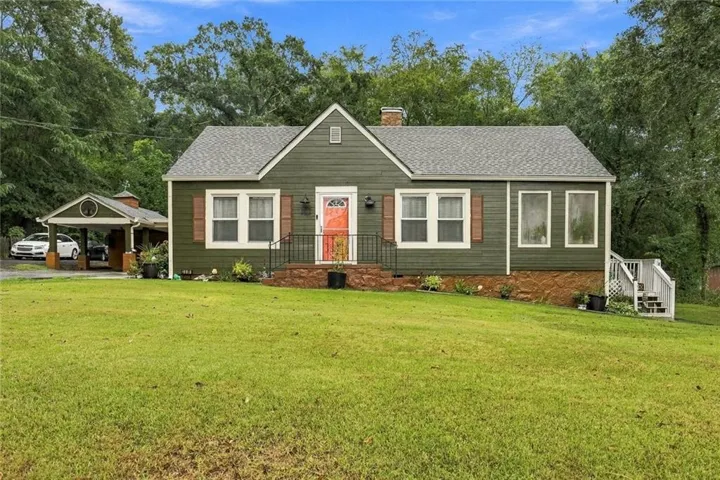 Green siding exterior with a contrasting orange front door, a covered carport, and a stone foundation accent