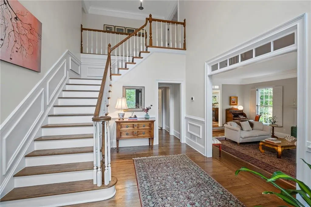 Stairway with crown molding, wood finished floors, a decorative wall, wainscoting, and a towering ceiling