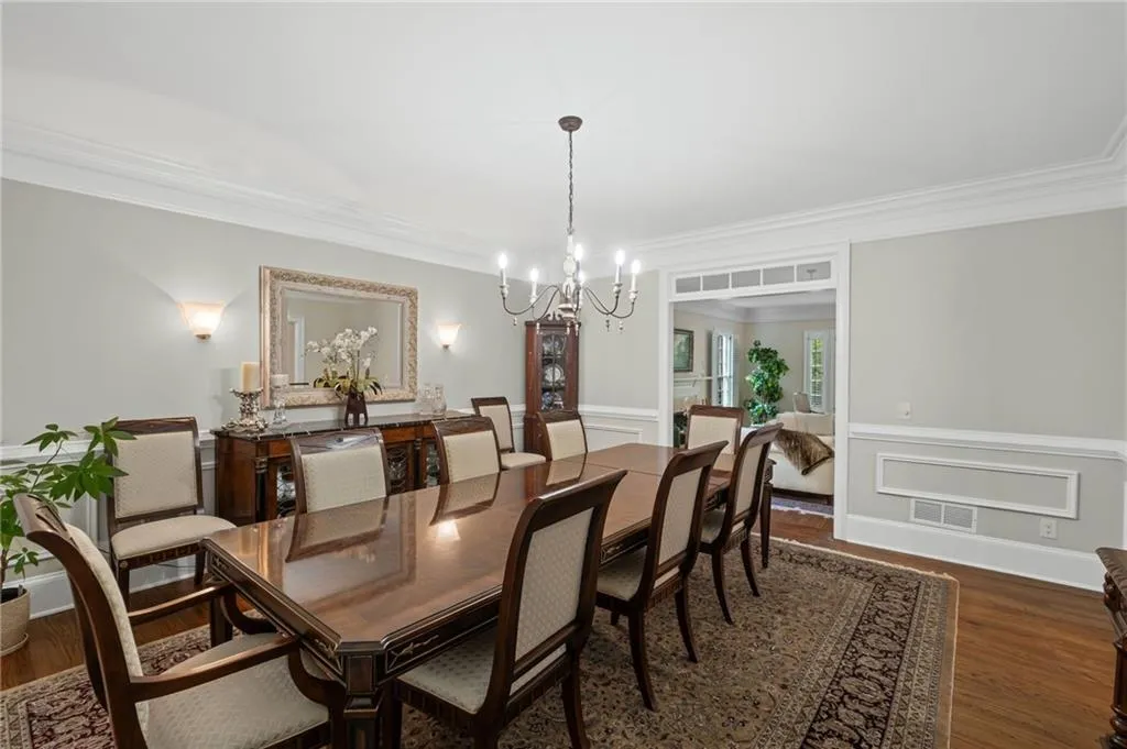 Dining space featuring dark wood-style flooring, ornamental molding, a chandelier, a decorative wall, and wainscoting