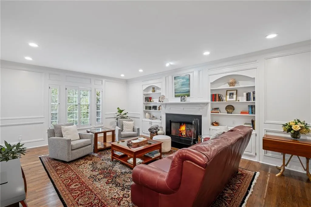 Living room with a decorative wall, a glass covered fireplace, recessed lighting, dark wood-style flooring, and crown molding