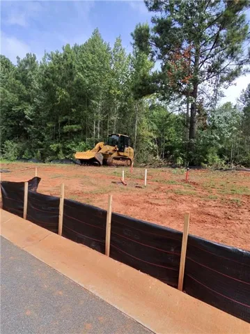 Cleared building site with established tree line, visible street curb, and erosion control fencing