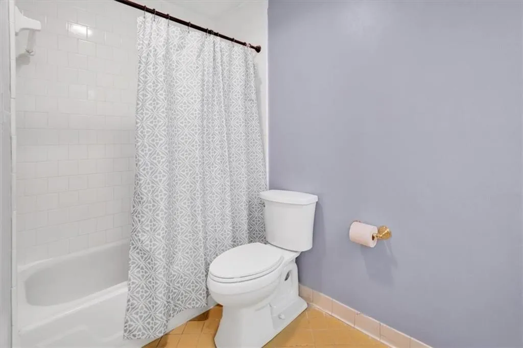 Bathroom with shower / bathtub combination with curtain, tile flooring, and toilet