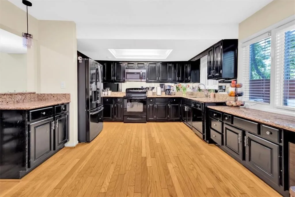 Kitchen with light hardwood / wood-style floors, appliances with stainless steel finishes, a tray ceiling, decorative light fixtures, and sink