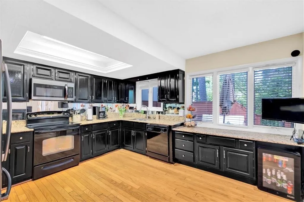 Kitchen featuring sink, a raised ceiling, light wood-type flooring, and black appliances