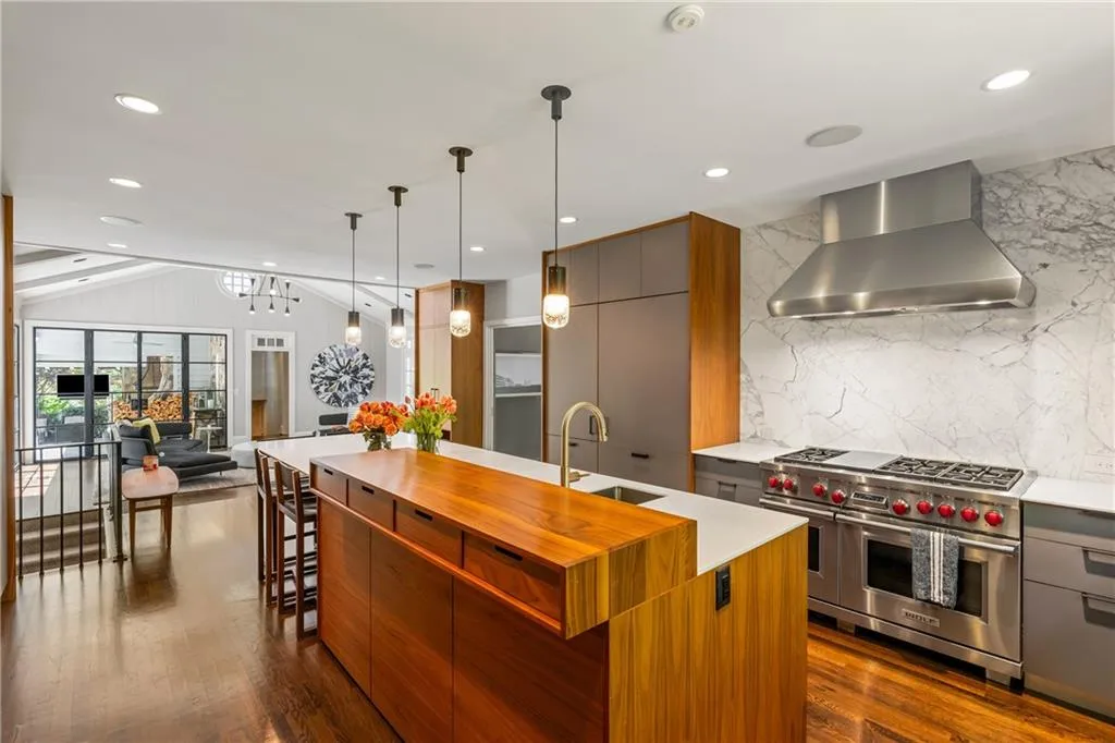 Kitchen with range with two ovens, wall chimney range hood, a sink, modern cabinets, and vaulted ceiling