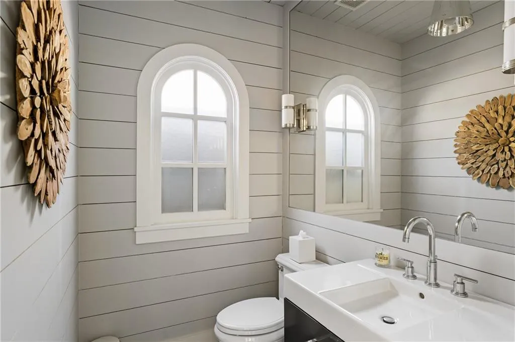 Bathroom featuring a sink, wood walls, toilet, and plenty of natural light