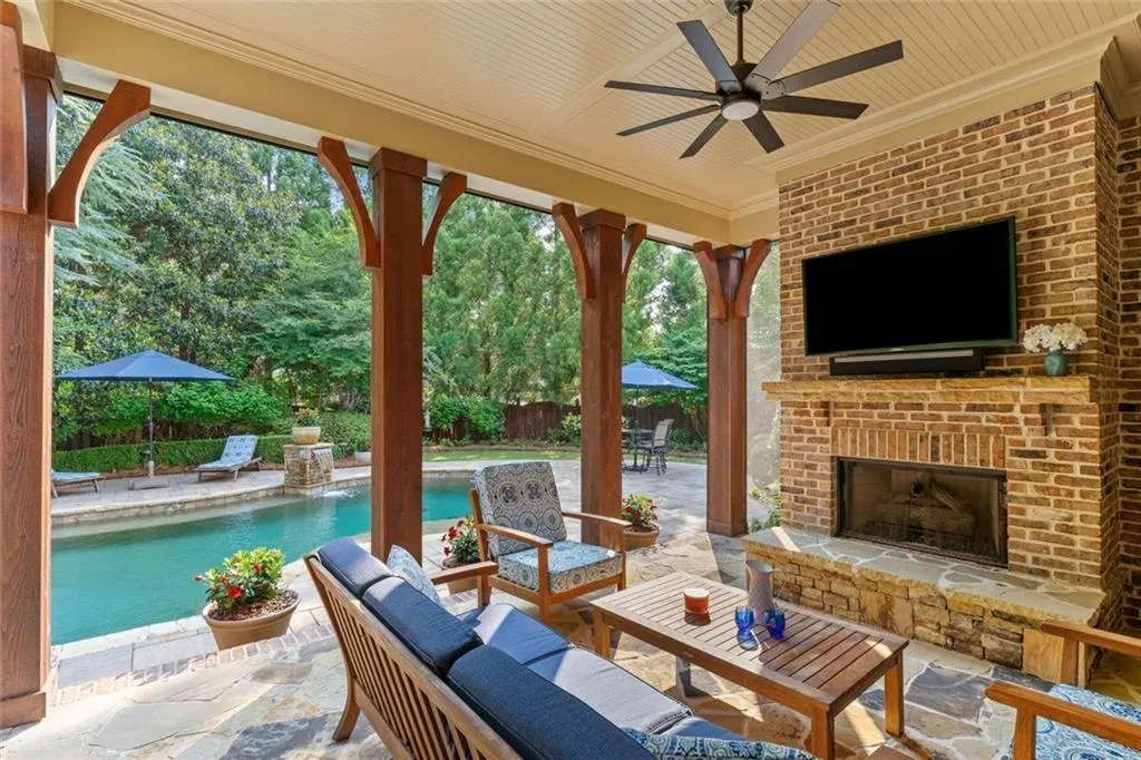 The covered patio with a cozy stone gas fireplace and SunBrite outdoor TV and Sonos sound bar create the perfect year-round outdoor living space with motorized retractable screens for bug-free evenings.