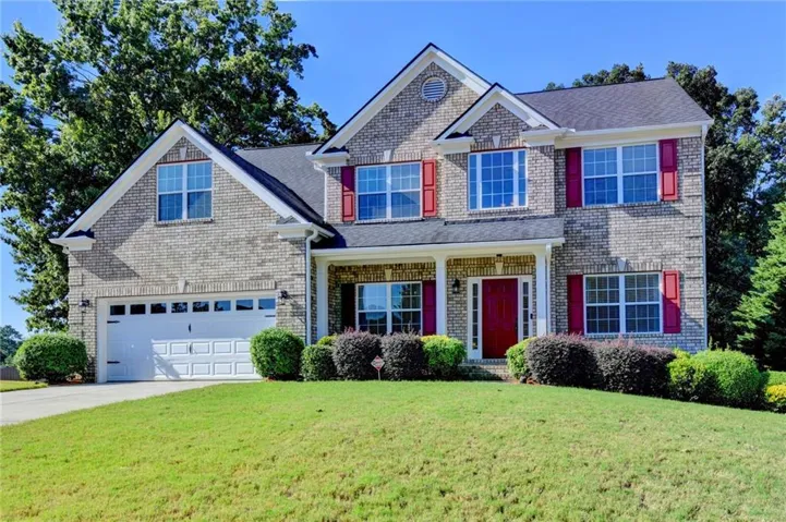 Brick facade home with a two-car garage, red front door, and accent shutters