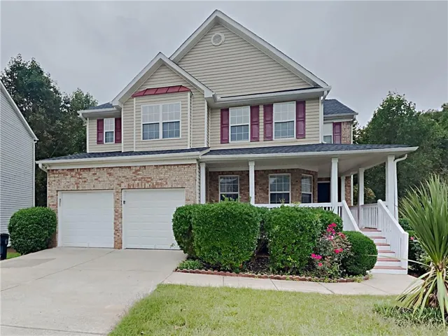 Two-story home featuring a combination brick and siding exterior, an inviting front porch with white columns, and a two-car garage