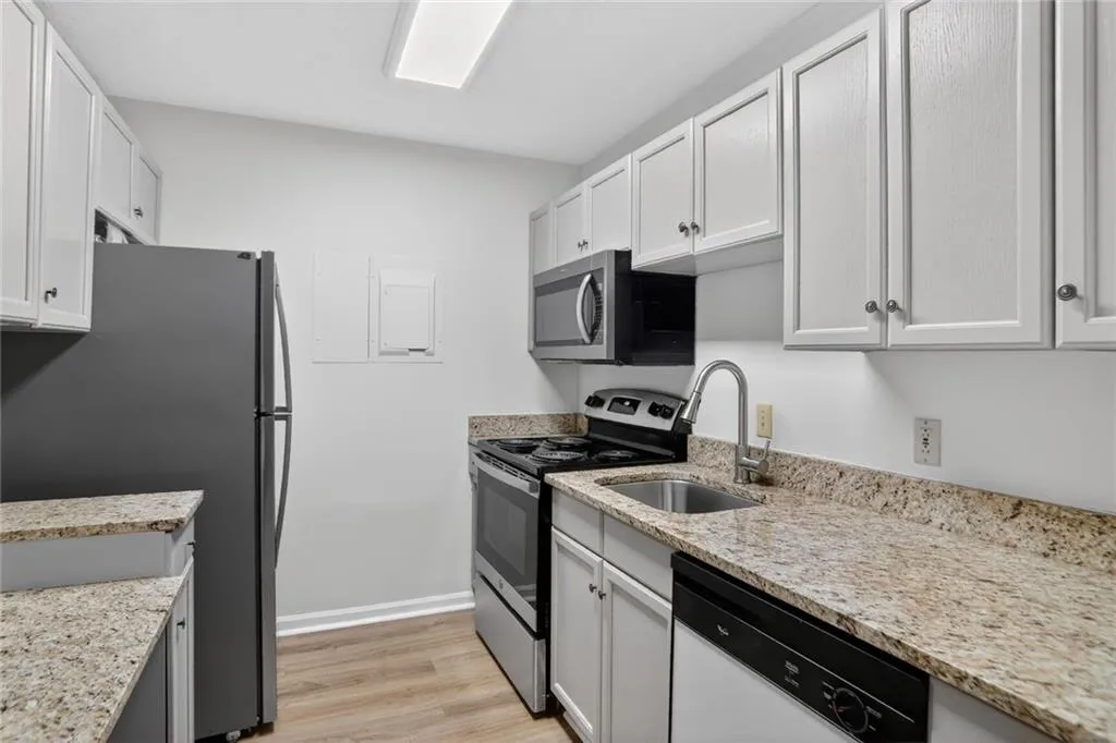 Kitchen featuring stainless steel appliances, light wood-type flooring, light stone countertops, and white cabinets