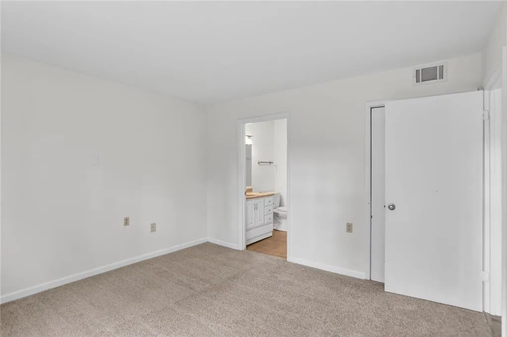 Unfurnished bedroom featuring light carpet and connected bathroom