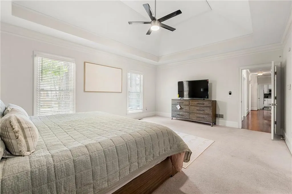 Bedroom featuring a raised ceiling, carpet flooring, baseboards, ornamental molding, and a ceiling fan