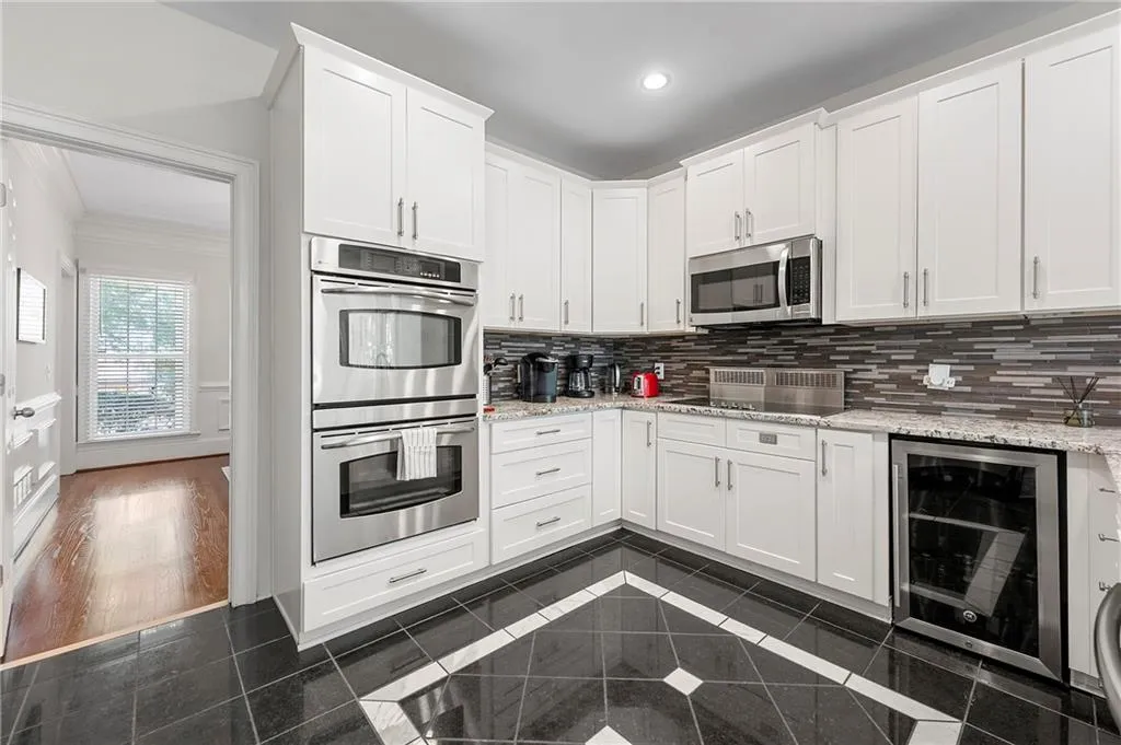 Kitchen featuring stainless steel appliances, beverage cooler, backsplash, white cabinetry, and crown molding