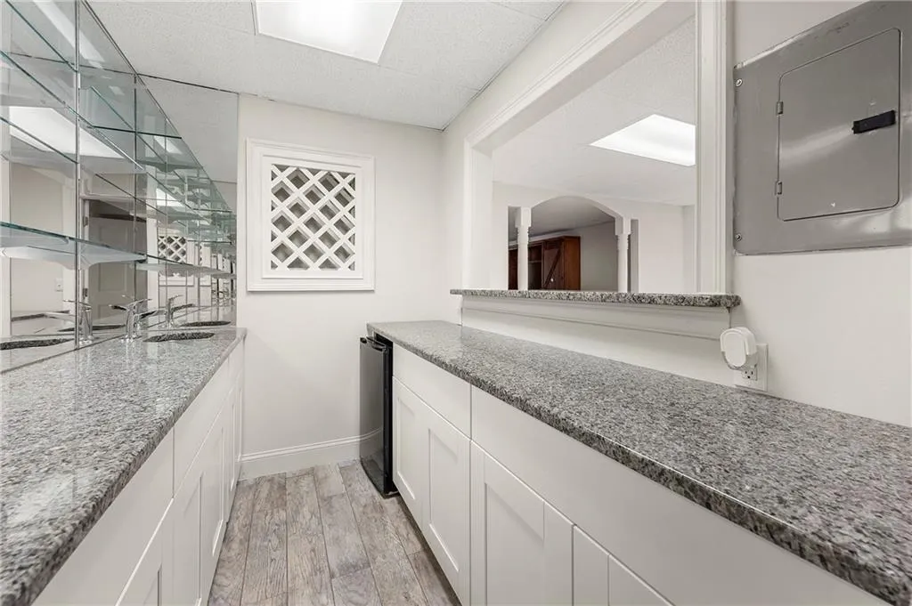 Indoor wet bar with electric panel, a paneled ceiling, light wood-style floors, baseboards, and arched walkways