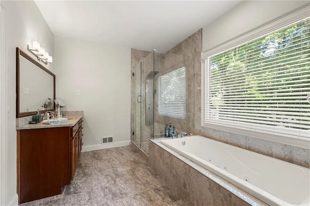 Bathroom with vanity, a stall shower, a tub with jets, and baseboards