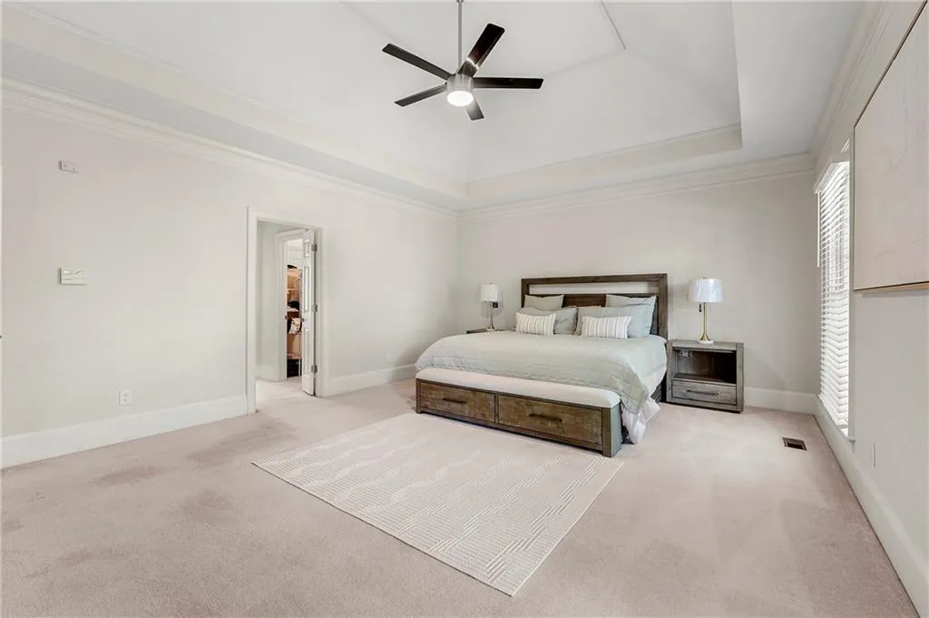 Bedroom with light colored carpet, a raised ceiling, baseboards, and ornamental molding