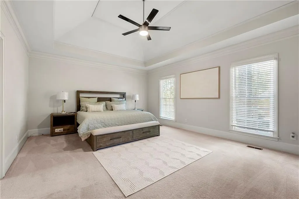 Carpeted bedroom with a raised ceiling, crown molding, baseboards, and ceiling fan